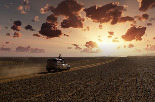 Offroad vehicle travels through vast desert at sunset, raising dust on a rugged trail under a dramatic sky with colorful clouds. Suitable for themes about adventure, road trips, exploration, outdoor activities, photography, travel blogs, and nature scenes.