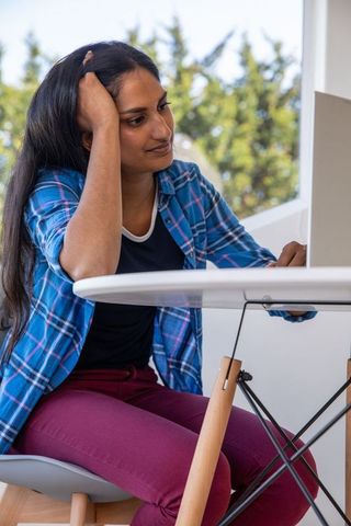 Young woman pondering over laptop outdoors on balcony