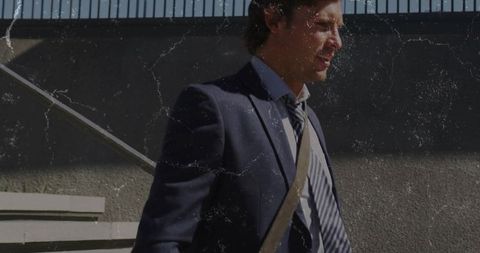 Sunlit businessman walking down concrete staircase carrying tan leather shoulder bag urban