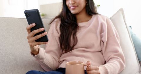 Relaxed woman with smartphone and coffee on couch