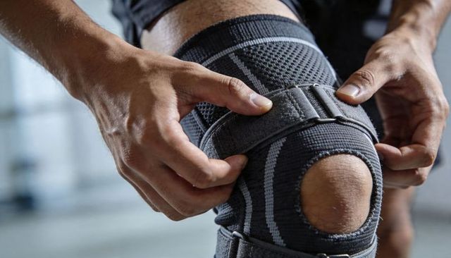 Male athlete adjusting open-patella knee brace with velcro straps for workout support