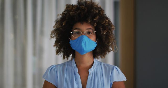 Portrait of biracial woman with curly hair wearing blue face mask. out and about during coronavirus covid 19 pandemic.