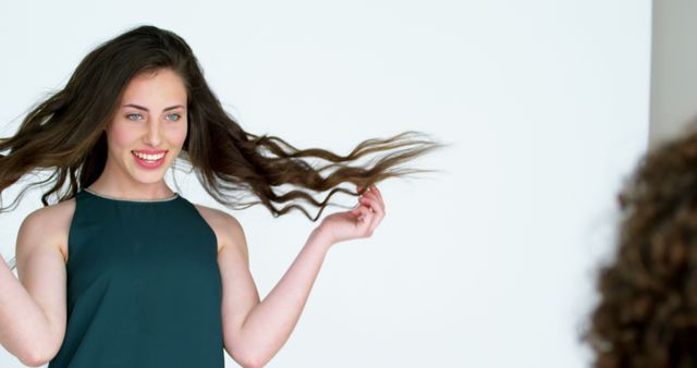 A young Caucasian woman is playfully twirling her long brown hair, with copy space. Her joyful expression and dynamic hair movement create a lively and vibrant atmosphere.
