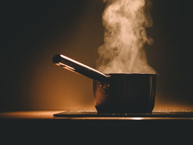 Visible on a wooden kitchen counter, steam emerging from a sturdy metal saucepan under warm, ambient lighting. Perfect for food blogs, cooking articles, or kitchen-related advertising. Captures the warmth and homely feel of cooking at home.
