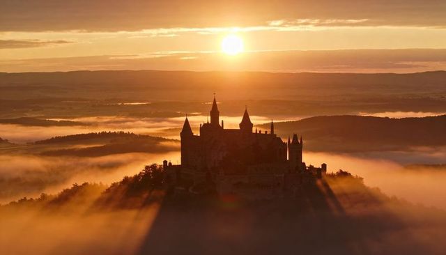 Sunrise bathing medieval castle on misty hilltop casting long radial shadows golden dawn
