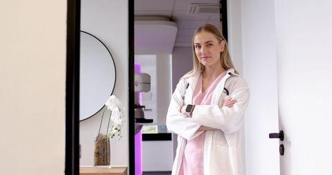Confident clinician standing in clinic doorway wearing white coat and pink scrubs
