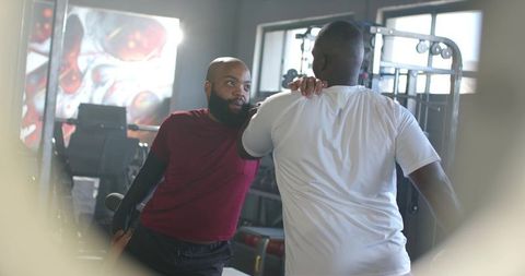 African men training with personal trainer guiding shoulder placement during cable workout