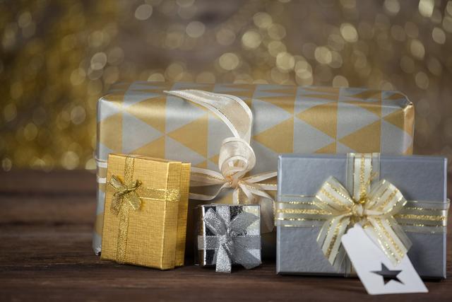 Close-up of beautifully wrapped gift boxes in gold and silver paper with ribbons on a wooden table. Ideal for holiday-themed promotions, Christmas advertisements, festive greeting cards, and seasonal blog posts.