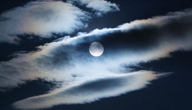 Glowing Full Moon Piercing Layered Wispy Clouds with Soft Lunar Halo Over Night Sky