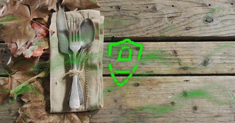 Placing rustic cutlery tied with twine on weathered wood with neon green shield emblem