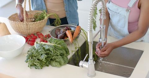 African american mother and daughter washing fresh vegetables together in bright kitchen