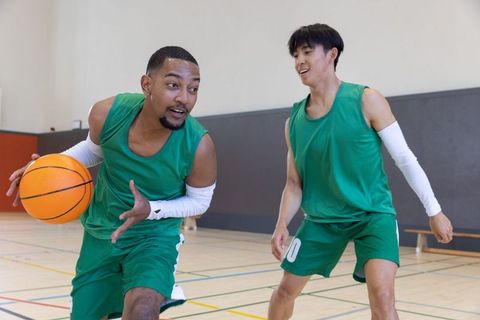 Teammates dribbling basketball on indoor court wearing green jerseys