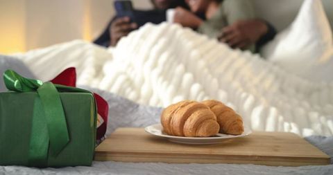 Cozy morning couple sharing croissant breakfast in bed with green gift box