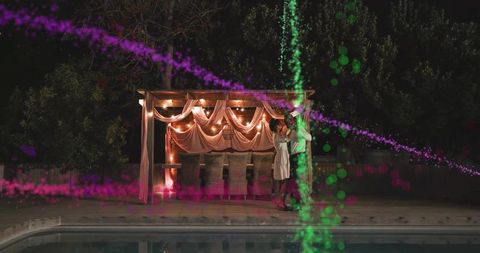 Romantic couple embracing on illuminated backyard pergola by pool at night, cinematic ambiance