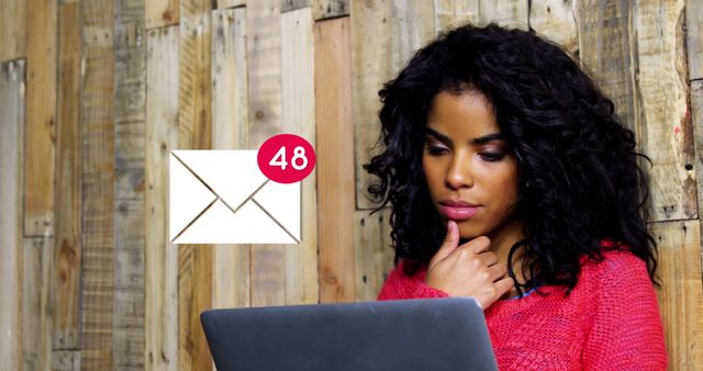 Digital composite of an African-american woman leaning on a wall made of wood and looking at her laptop. A message icon with numbers counting up is seen in the foreground 4k