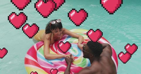 Couple smiling on colorful lollipop float in pool surrounded by pixel heart graphics fun