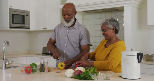 This image shows an African American senior couple joyfully chopping vegetables together in a bright, home kitchen. Ideal for websites and articles promoting healthy lifestyles, senior living, family bonding, nutrition education, cooking classes, or retirement community advertisements. It emphasizes themes of domestic life, togetherness, and active living among elderly couples.