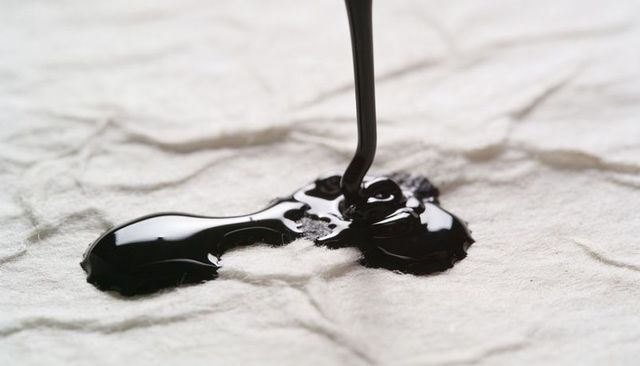 Pouring glossy black liquid on crumpled white fabric closeup with reflective puddle macro
