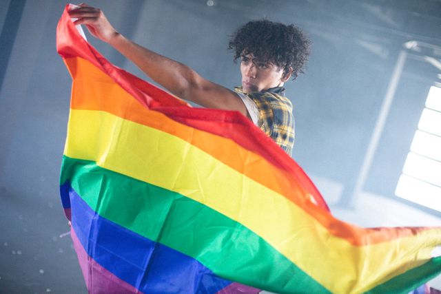 African american transgender man holding lgbt flag in empty parking garage. concept of gender expression, identity and diversity.