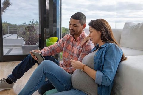 Pregnant Couple Relaxing Together Looking at Tablet in Modern Home
