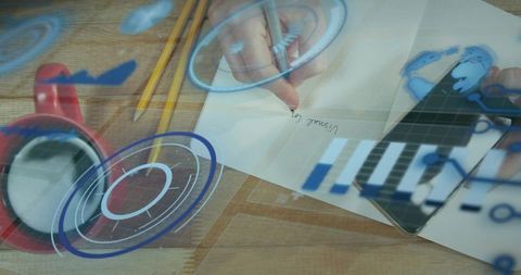 Hands writing notes and tapping tablet with augmented hud overlay on wooden desk workspace