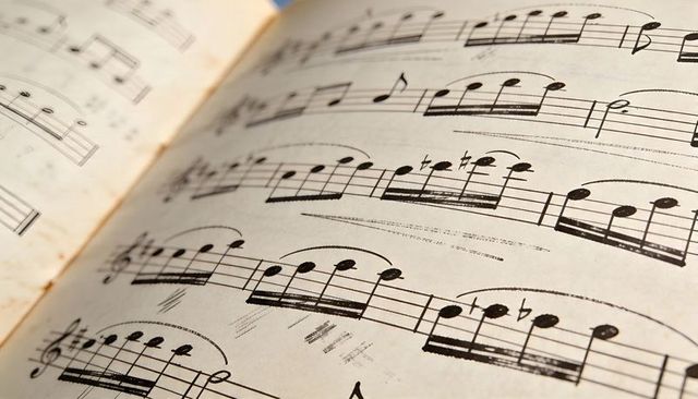 Vintage classical sheet music closeup showing curved score and printed notation with binding crease
