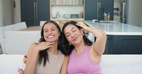 Diverse friends relaxing and smiling on couch touching hair in modern open-plan kitchen interior