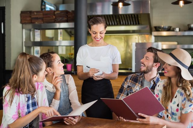 Waitress taking orders from a group of happy customers in a restaurant. Ideal for use in hospitality industry promotions, restaurant advertisements, customer service training materials, and dining experience blogs.