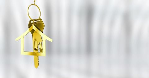 Hanging gold house keychain holding brass keys on pale gray backdrop with copy space