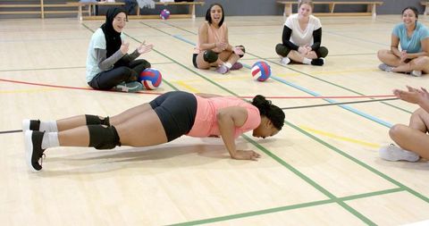 Multicultural female volleyball team cheering teammate doing pushups during training