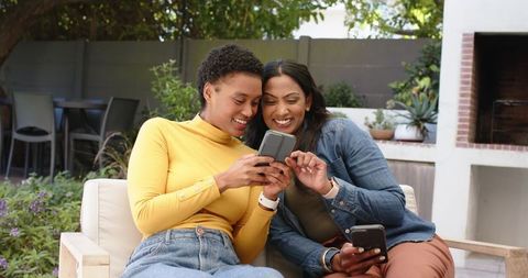 Diverse friends exploring smartphone outside on sunny patio