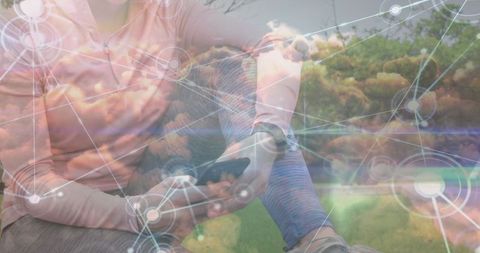 Tech savvy woman in park using smartphone and smartwatch with digital network