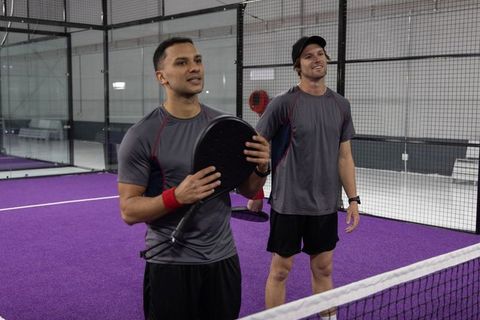 Duo playing padel on indoor purple court holding paddles and smiling