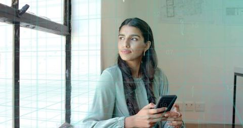 Professional Woman Analyzing Data on Smartphone by Office Window