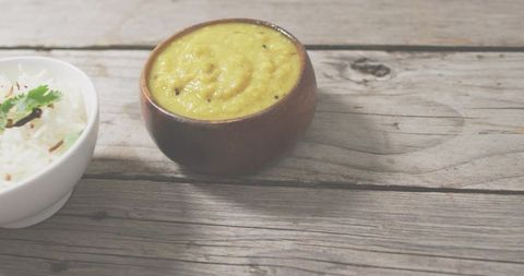 Yellow dal curry in clay bowl on rustic wood with steamed rice, minimal vegan comfort food
