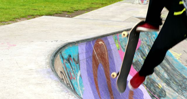 A skateboarder performs an airborne trick in a vibrant and colorful skate park. The graffiti on the ramps adds to the urban and dynamic feel of the scene, reflecting youth culture and extreme sports. The image is ideal for promoting skateboarding events, illustrating articles on youth activities or street culture, and can be used in advertisements for sports equipment.