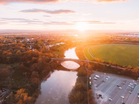 River reflecting golden sunset over arched bridge with glowing fields and parking lot
