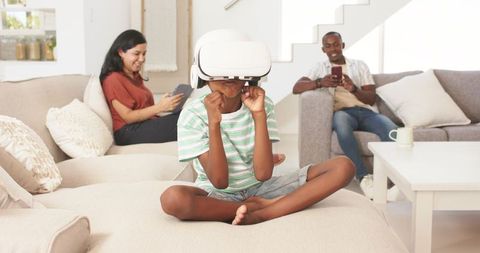 Child Wearing VR Headset Playing on Couch While Parents Using Devices in Bright Living Room