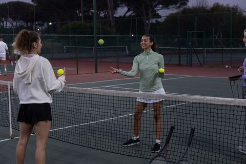Women practicing tennis volleys at dusk on outdoor hard court by net with rackets and balls