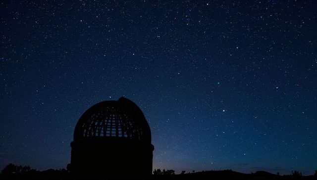 Observatory dome silhouette under starry night sky with open dome and rural horizon