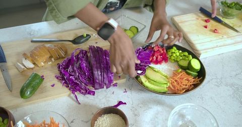Assembling colorful vegan grain bowl with purple cabbage avocado cucumber and edamame
