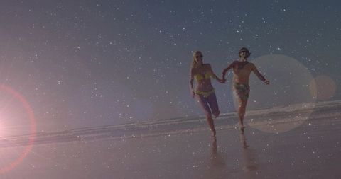 Couple running hand-in-hand on wet shoreline at sunset golden hour lens flare