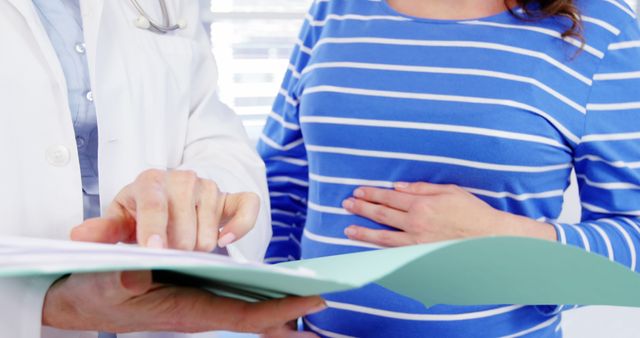 A Caucasian middle-aged female doctor is discussing medical records with a pregnant Caucasian young woman, with copy space. Their interaction underscores the importance of prenatal care for expectant mothers.