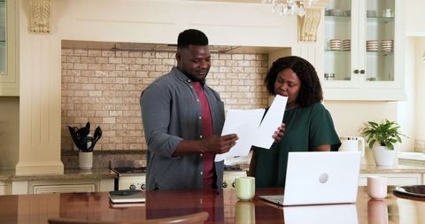 Mature Couple Reviewing Documents in Kitchen with Laptop