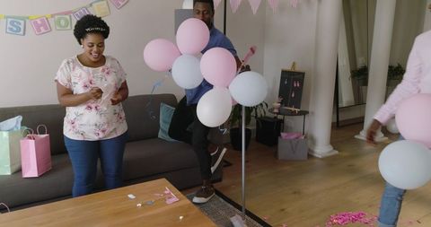 African american friends celebrating baby shower decorating living room with pink balloons