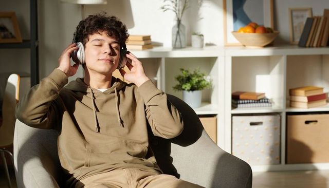 Sunlit teen relaxing in armchair listening to music with headphones cozy home interior