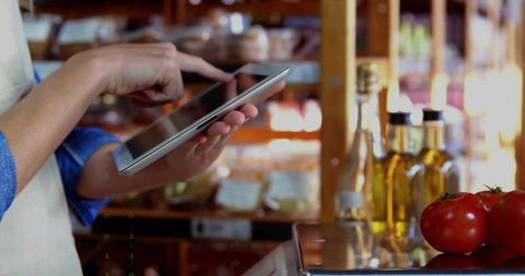 Shop Assistant Using Tablet at Deli Counter with Fresh Produce