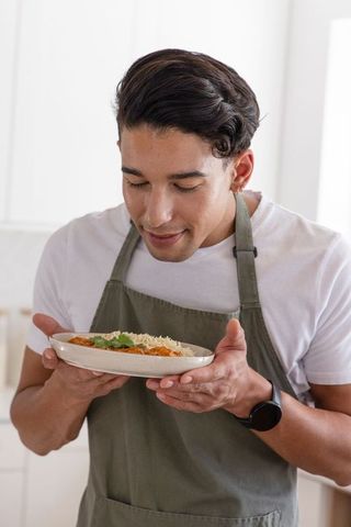 African american man smelling homemade curry and rice while wearing olive apron in bright kitchen