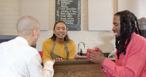Barista serving coffee to smiling customers at cozy cafe counter during friendly conversation