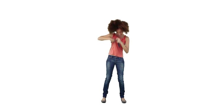 Woman passionately singing into a microphone, standing against a white background. Wearing casual attire with jeans and a sleeveless top, the scene exudes energy and fun. Perfect for use in music-related promotions, advertisements, or articles about performing arts and entertainment.